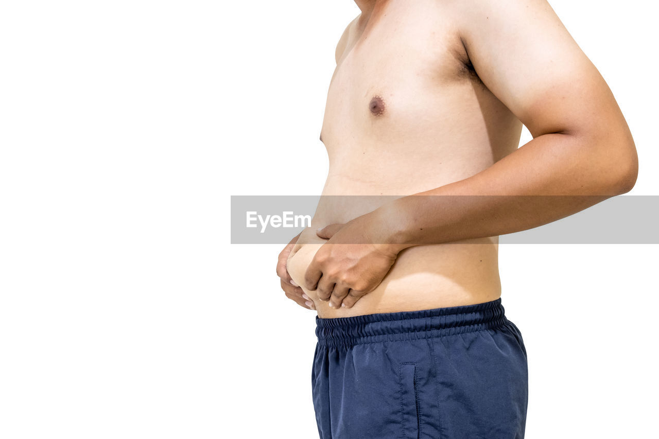 Midsection of shirtless man touching stomach against white background