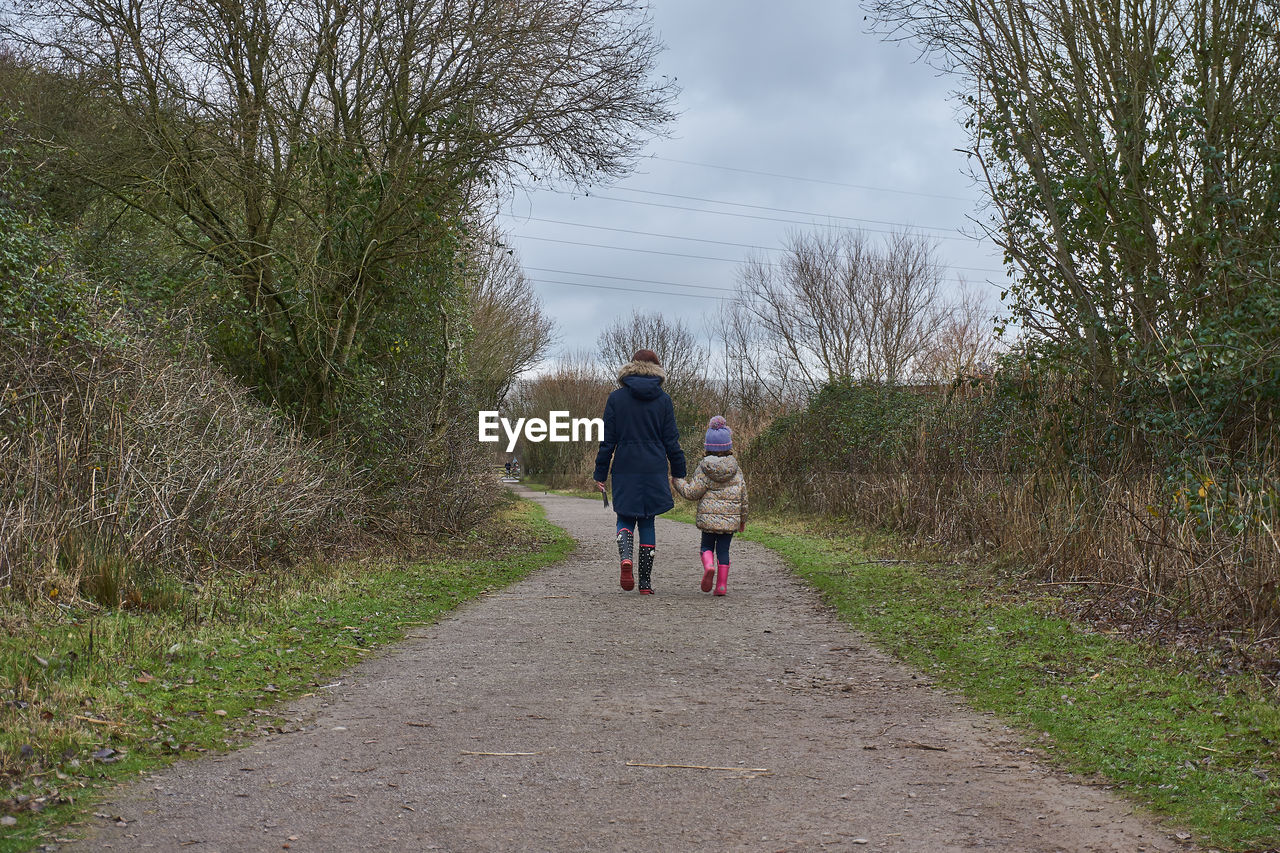 Rear view of mother and daughter walking on footpath amidst trees