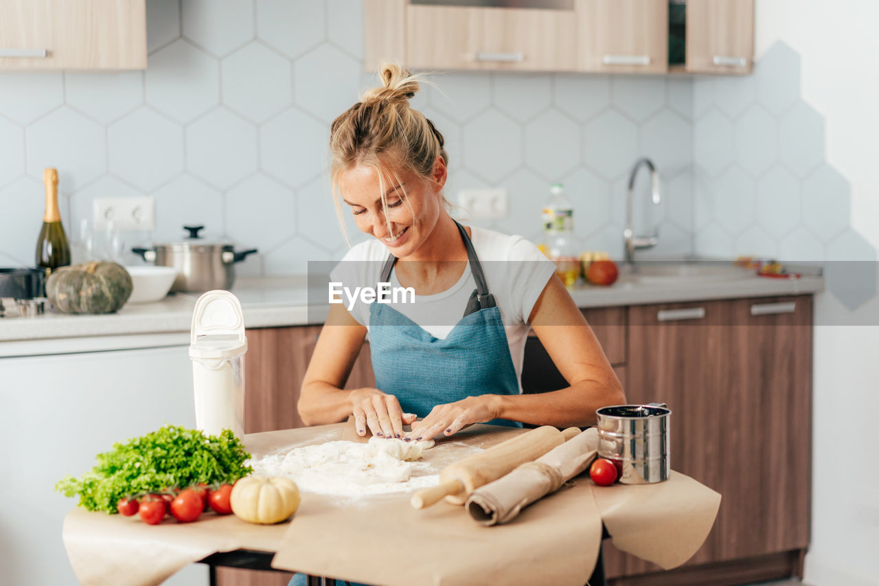 Young woman prepares dinner from ingredients of vegetables and dough at the table in the kitchen.