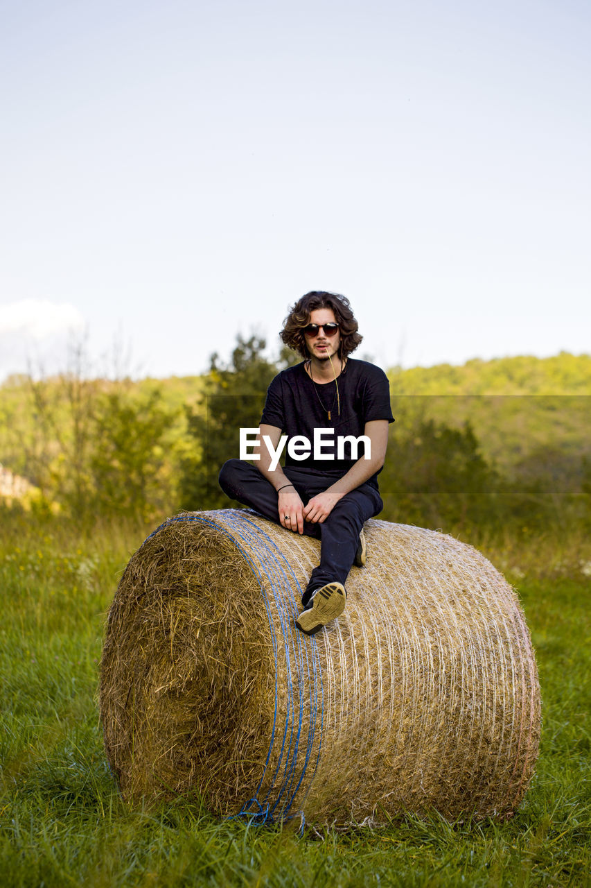 Portrait of man sitting on hay bale against sky