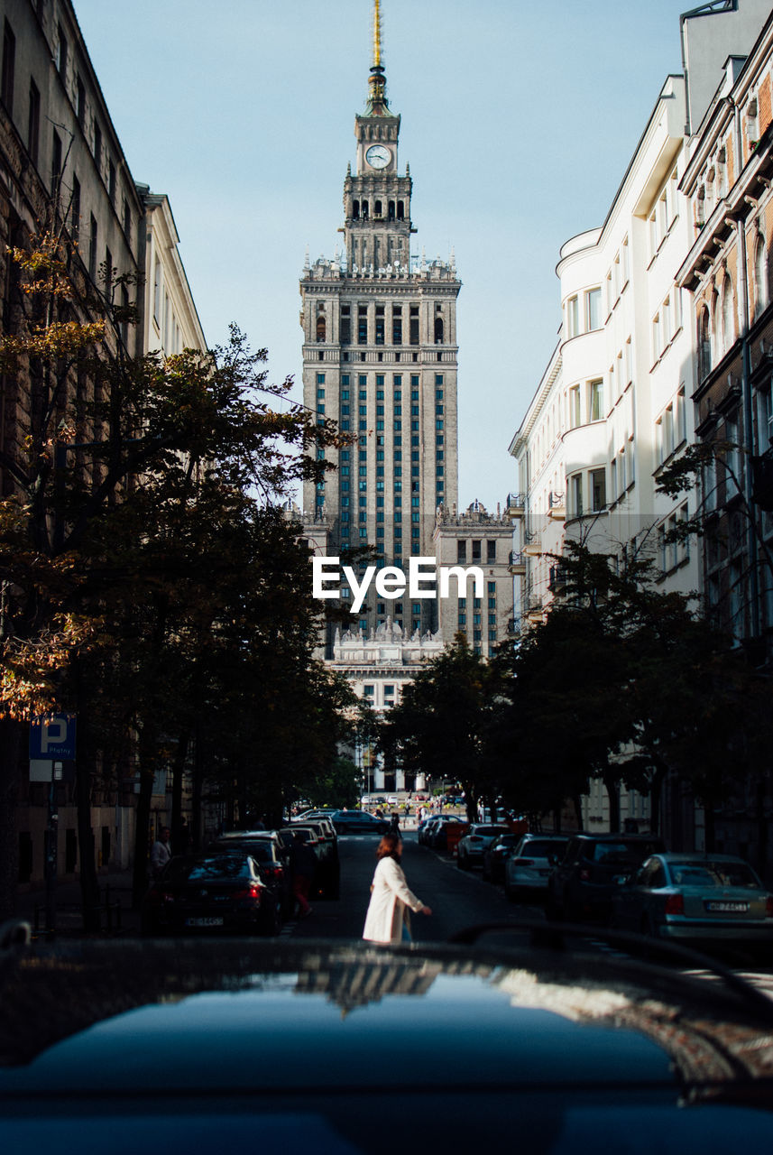 Woman crossing road with tower in background at city