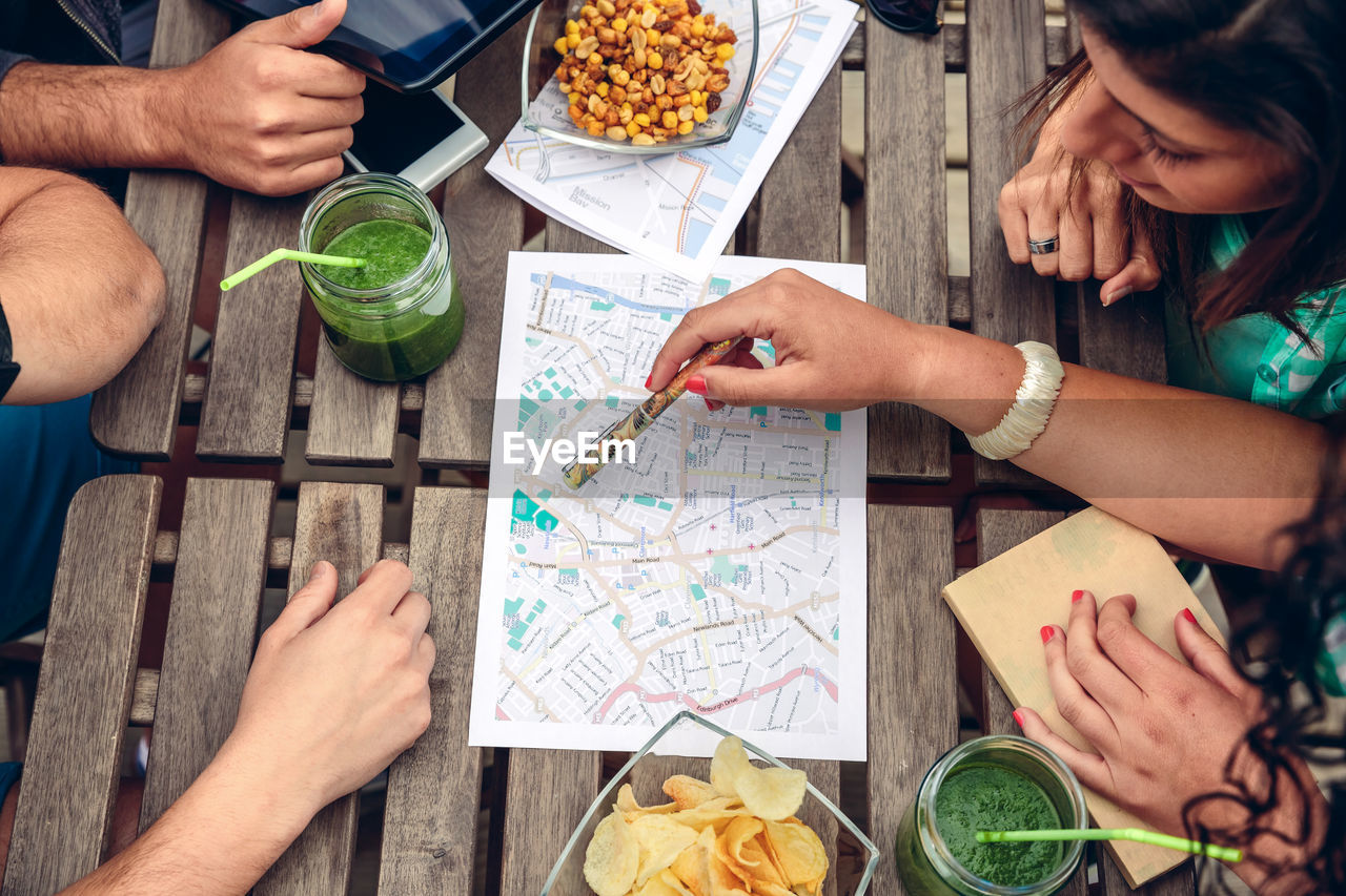 High angle view of friends discussing on map while sitting in restaurant