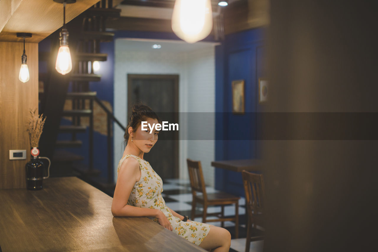 Portrait of young woman by table at restaurant