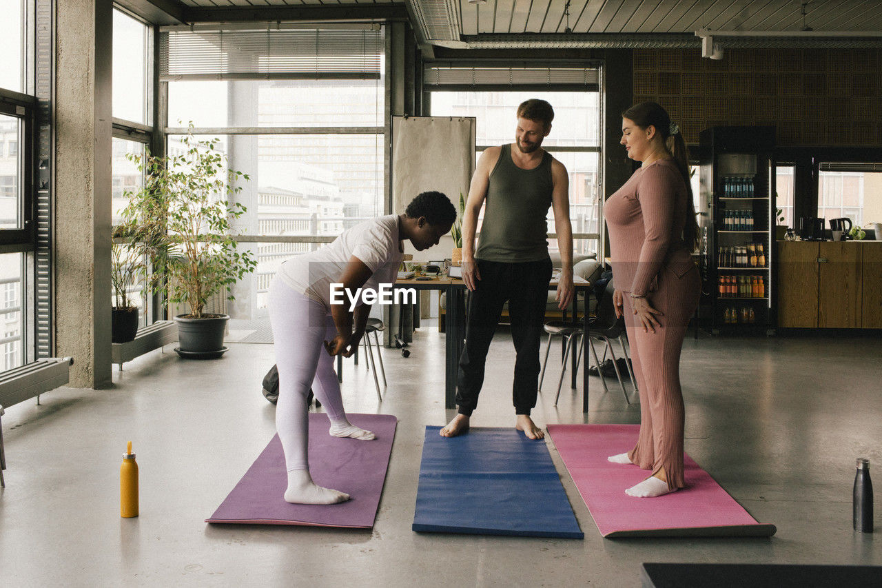 Full length of colleagues learning yoga from businesswoman at office