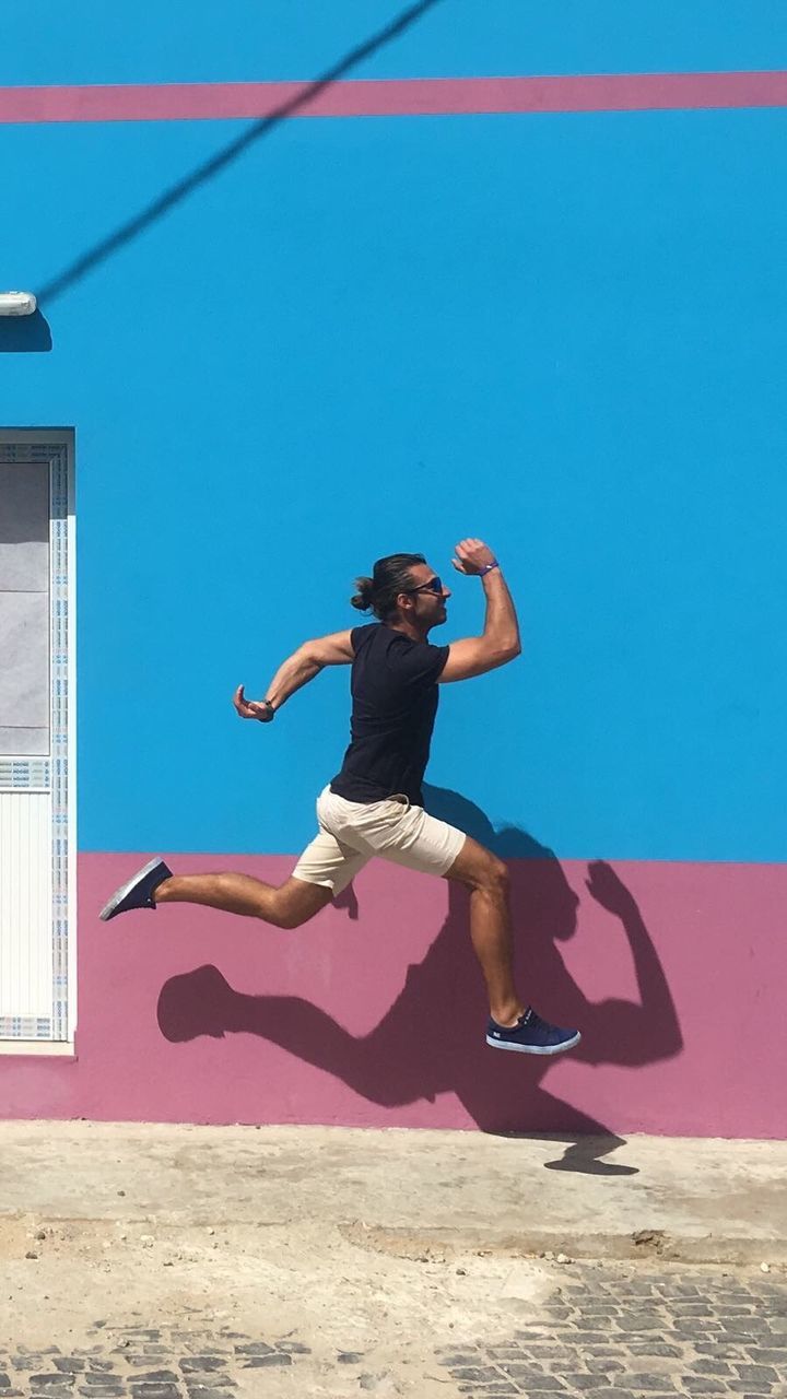 Side view of man levitating against colorful wall on sunny day