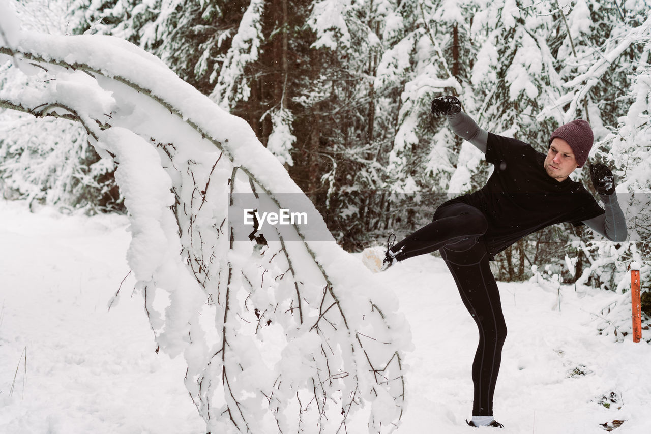 Man kicking snowy tree