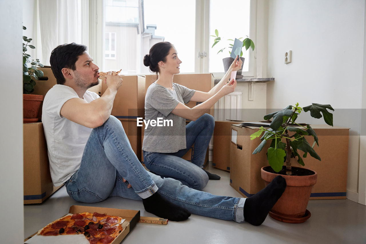 Man eating pizza while looking at woman choosing color swatches in new house