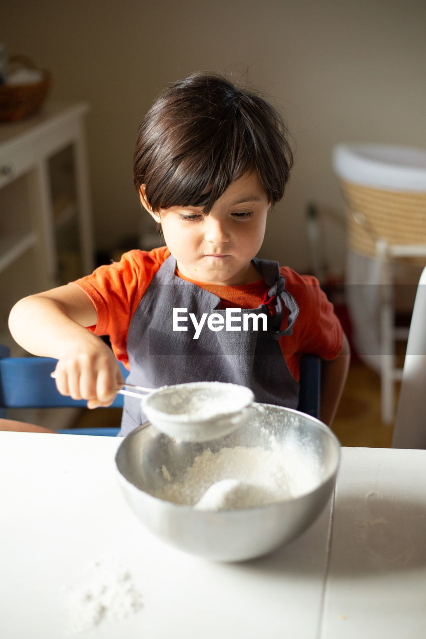 Child wearing grey apron sifting flour