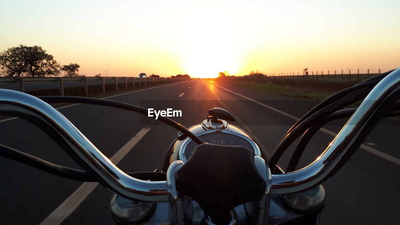 Cropped image of motorcycle handle against sky during sunset