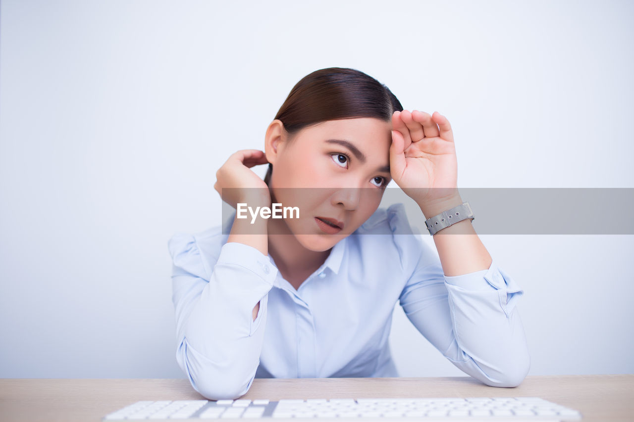 Tired businesswoman looking away sitting against wall