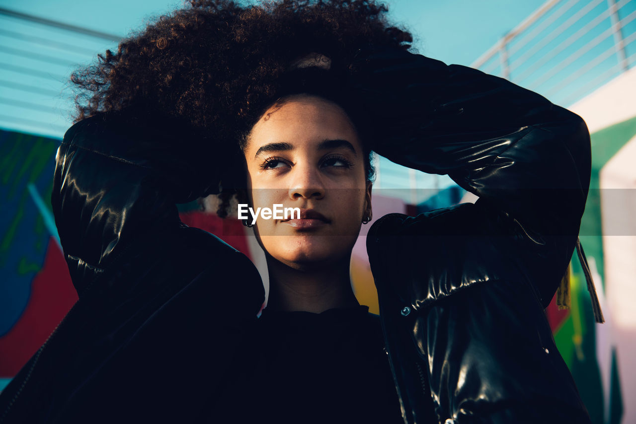 Stylish african american female with afro hairstyle in trendy black outfit standing on the street