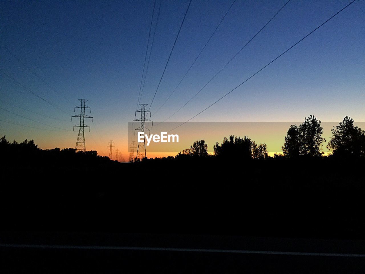 SILHOUETTE OF ELECTRICITY PYLONS ON LANDSCAPE