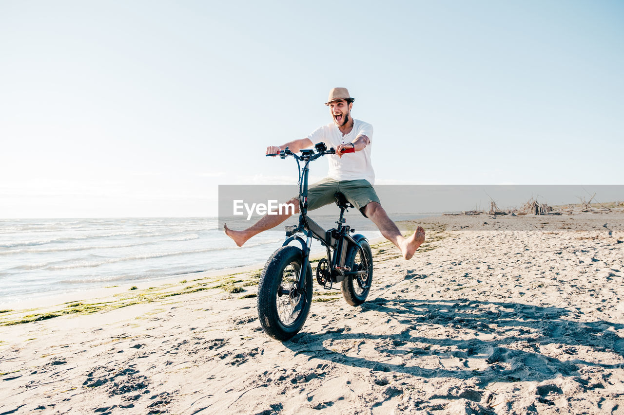 full length of woman riding bicycle on beach against sky