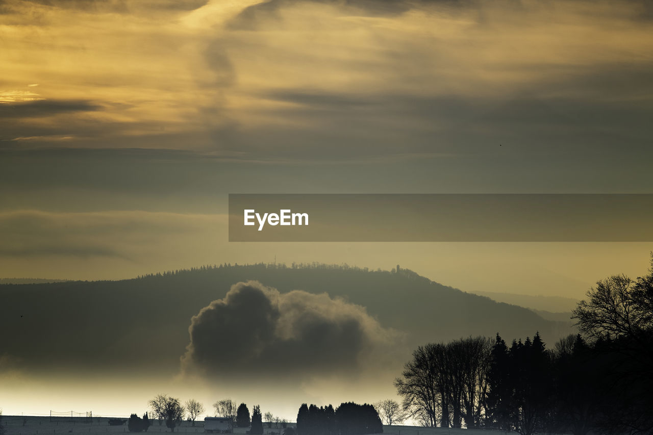 Silhouette trees against dramatic sky during sunset