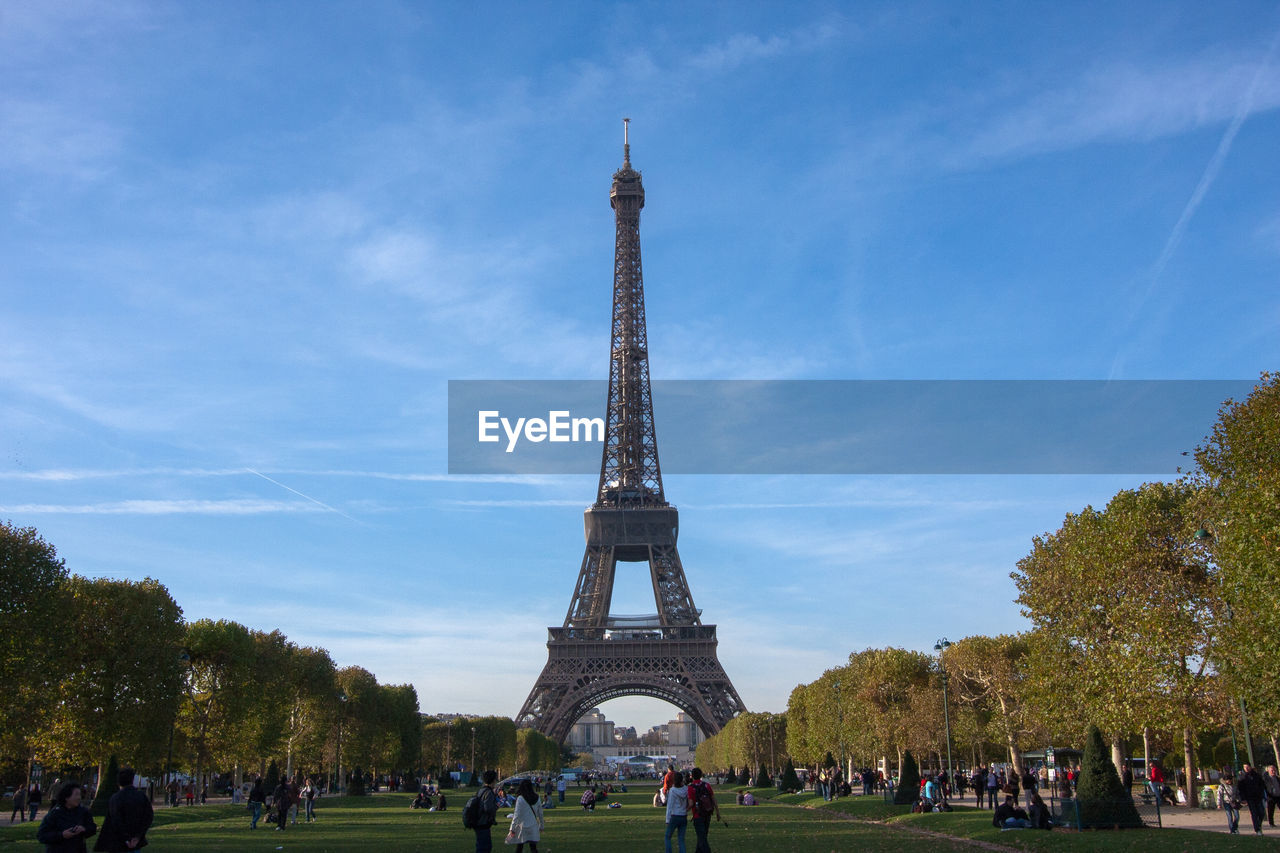 People at champ de mars by eiffel tower against sky