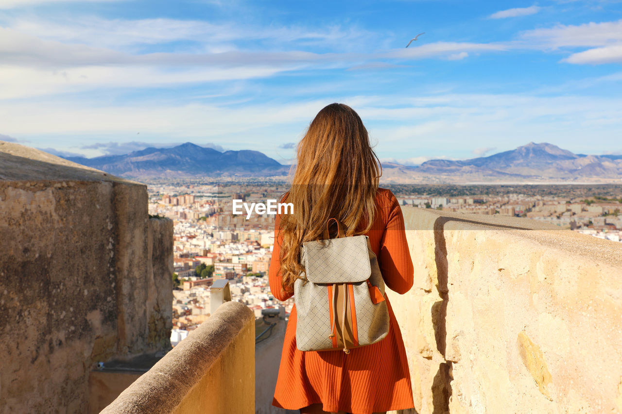 Rear view of woman carrying backpack while standing against sky