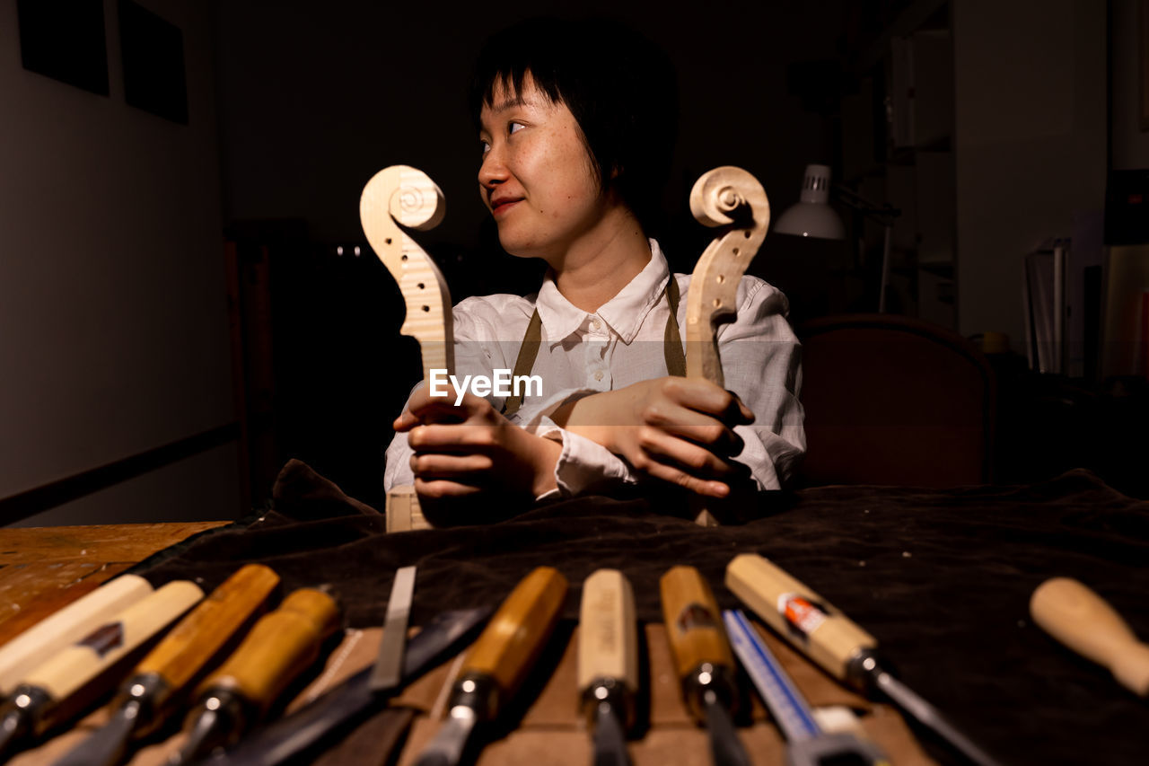 Young chinese woman violin maker showing the neck of the violins under construction in her workshop