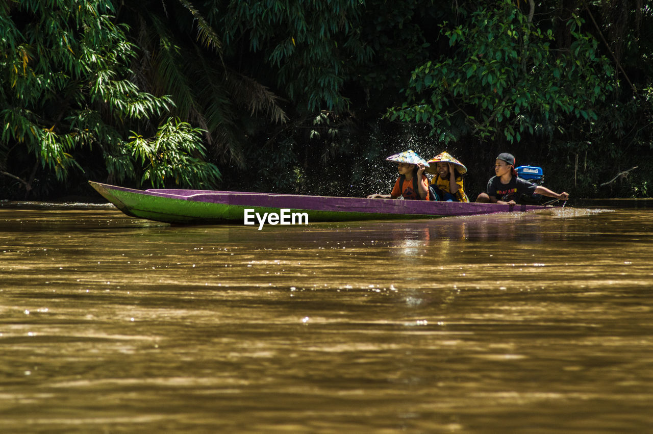 PEOPLE SITTING ON BOAT BY TREES