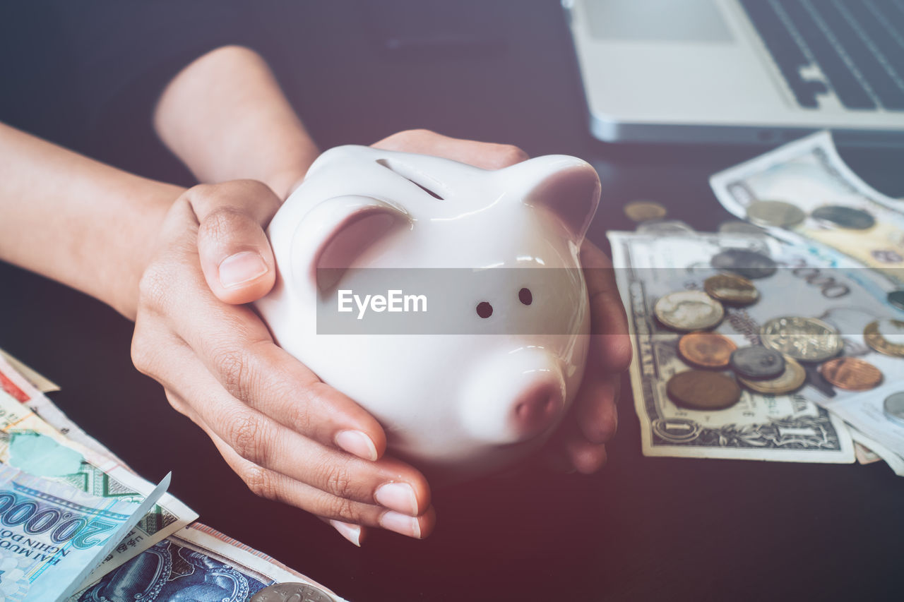 Cropped hands of businesswoman holding piggy bank on table