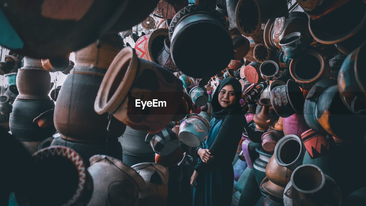 Portrait of woman wearing hijab standing amidst potteries at market