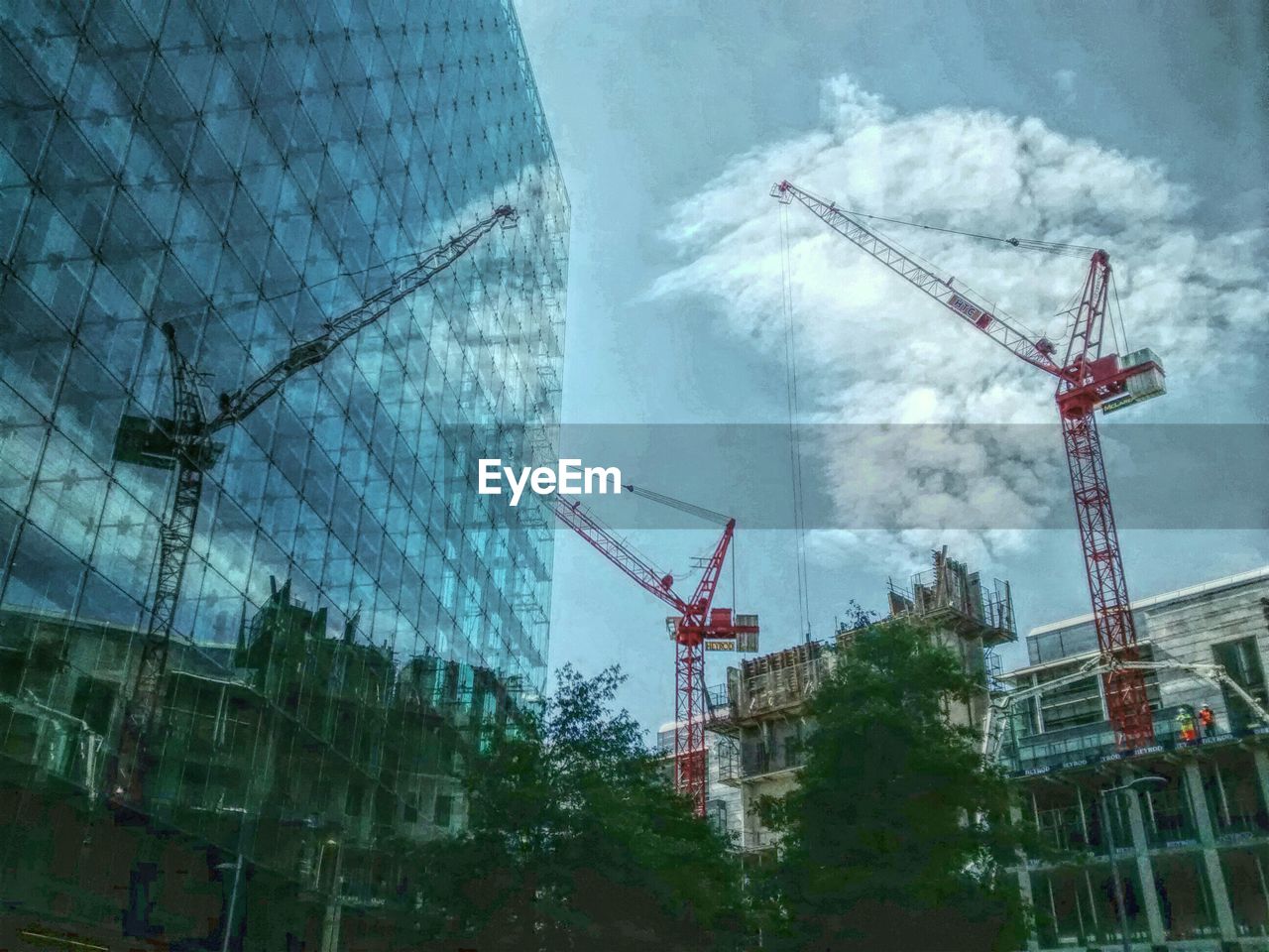 LOW ANGLE VIEW OF CRANES AGAINST CLOUDY SKY