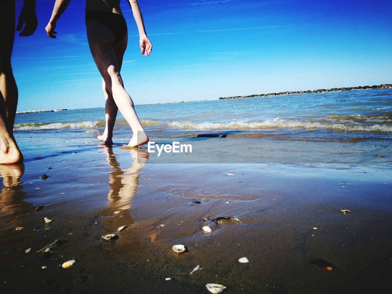 LOW SECTION OF WOMAN WALKING AT BEACH