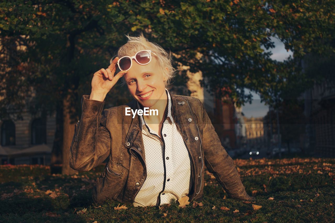 Portrait of mid adult woman holding sunglasses while standing against trees