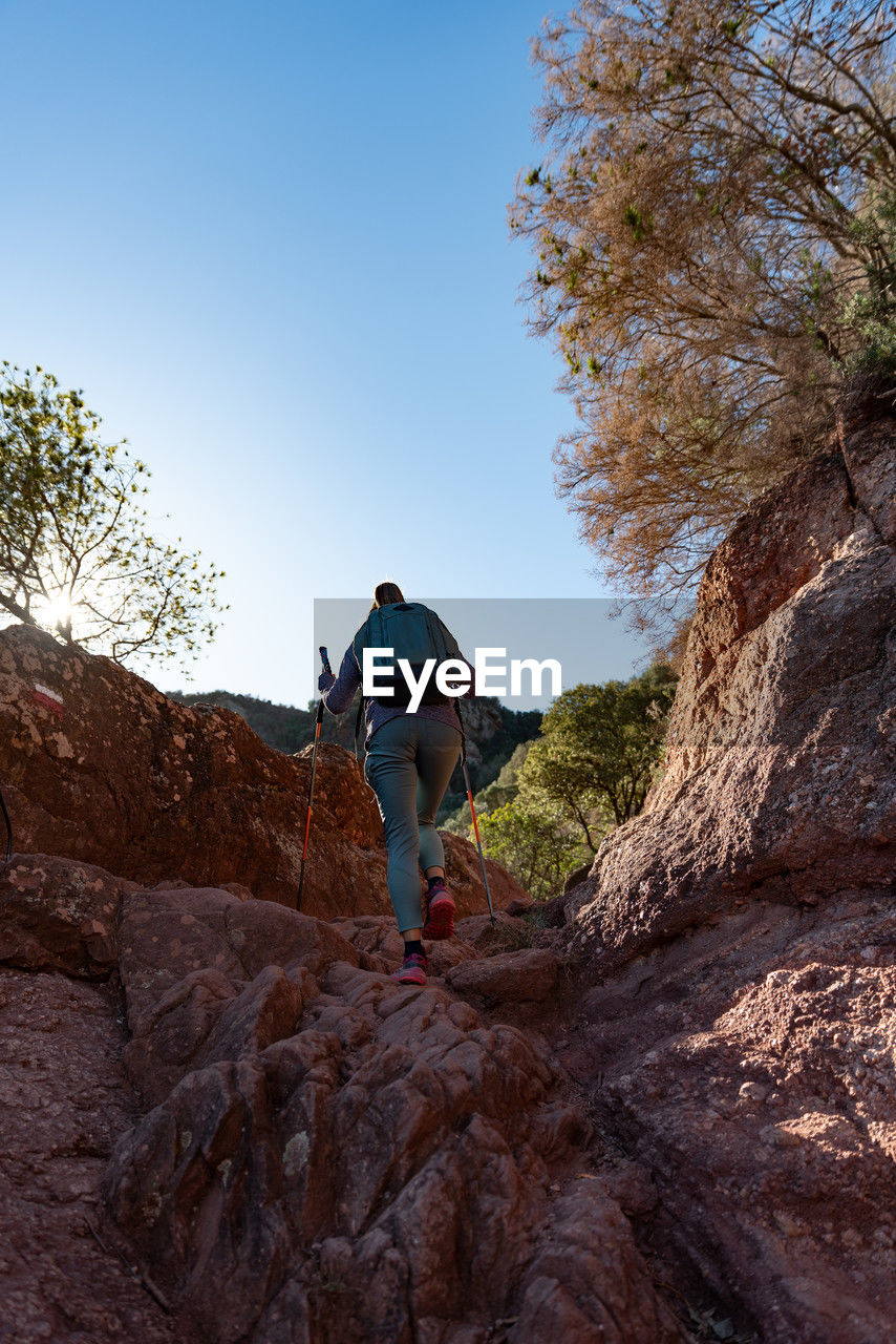 Woman climbs the mountain in the garraf natural park, supported by hiking sticks.