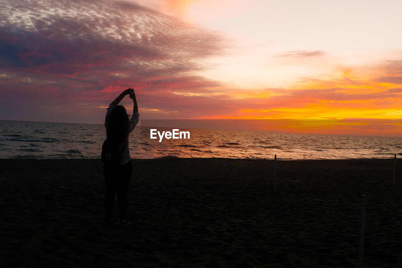 Silhouette woman at beach against cloudy sky during sunset