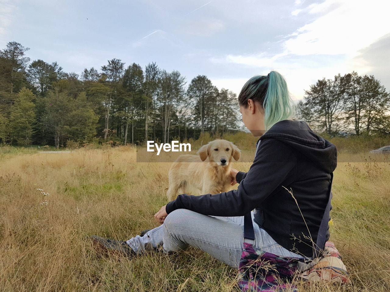 Rear view of woman with puppy sitting on field against sky