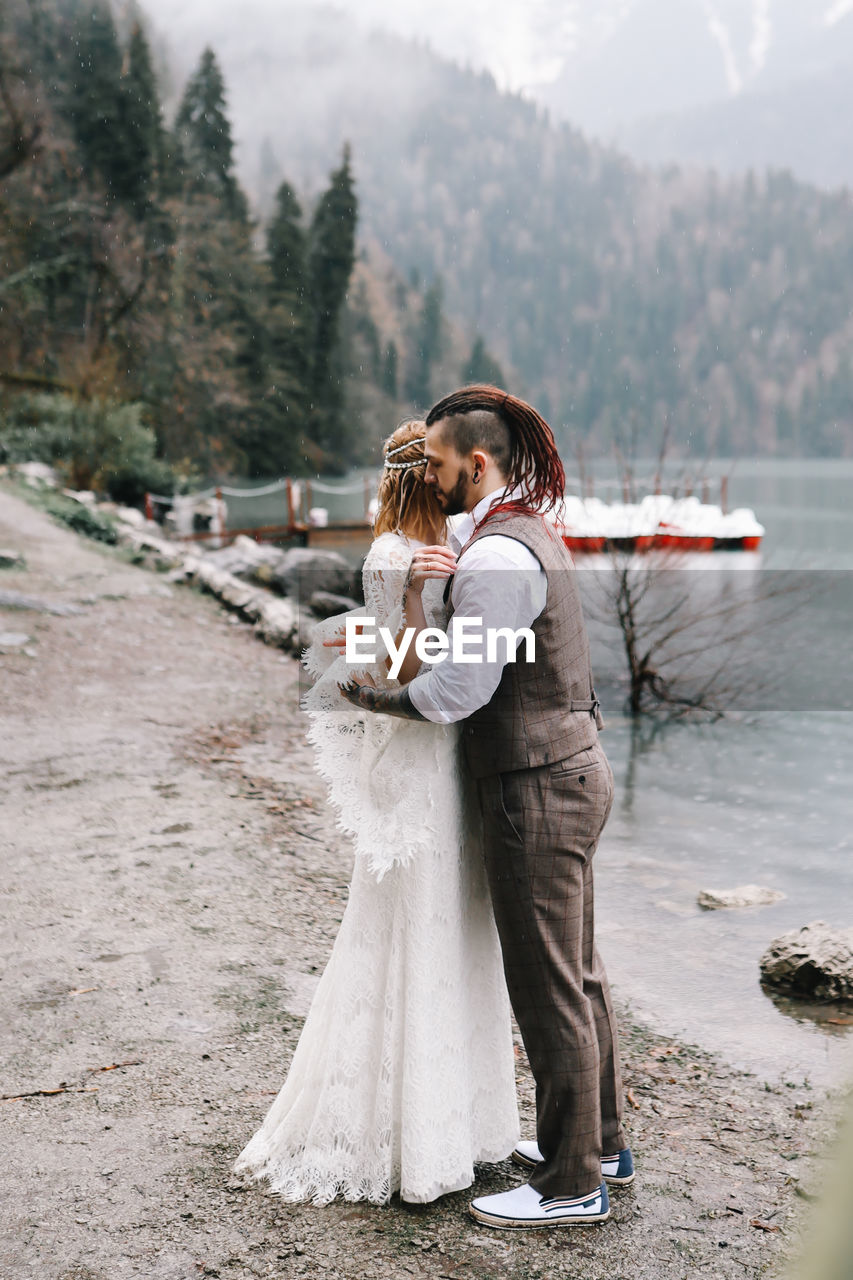 Happy newlyweds in love a man and a woman in wedding clothes embrace on the shore of the lake