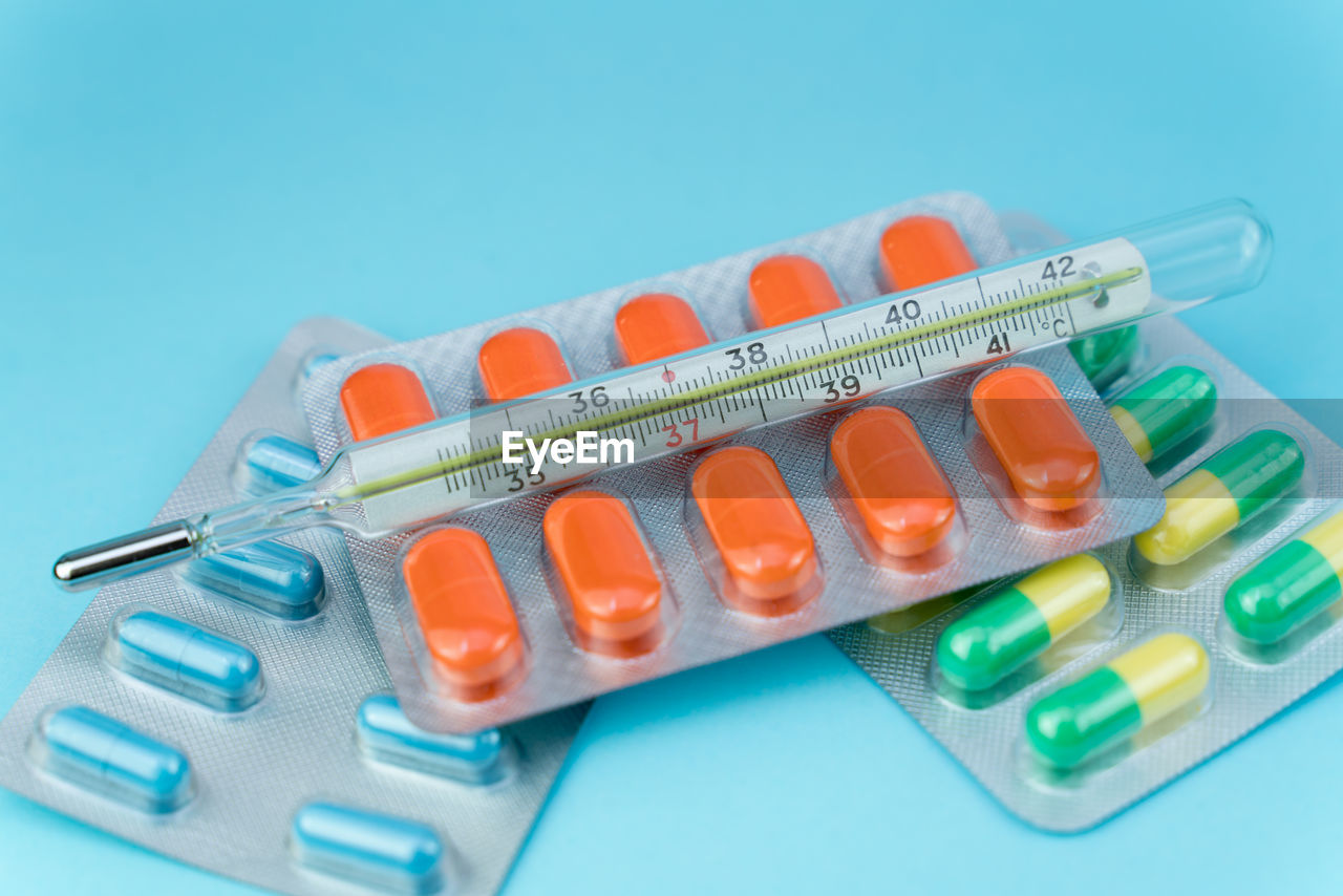 Blisters with pills and thermometer lie on a blue background closeup