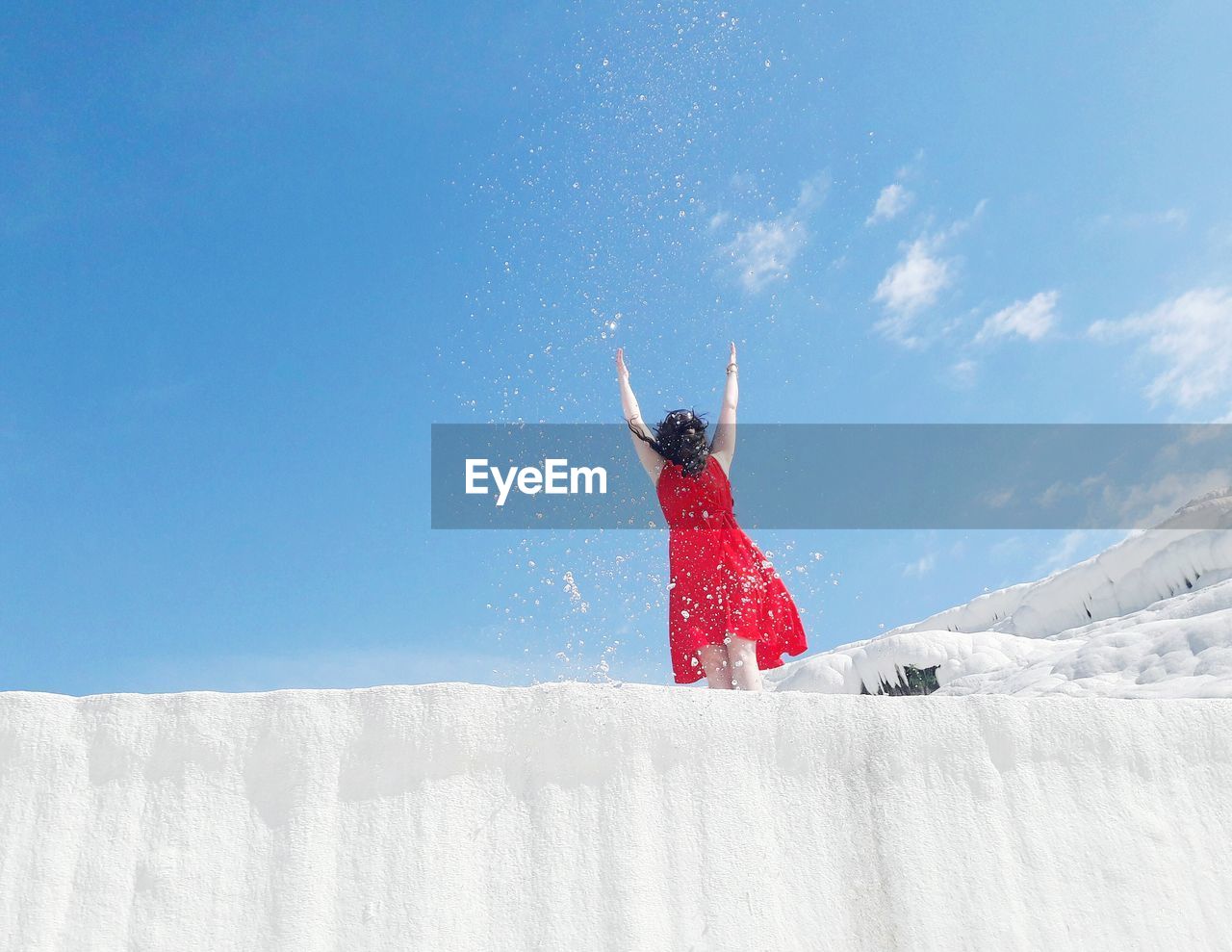 Woman throwing snow against blue sky