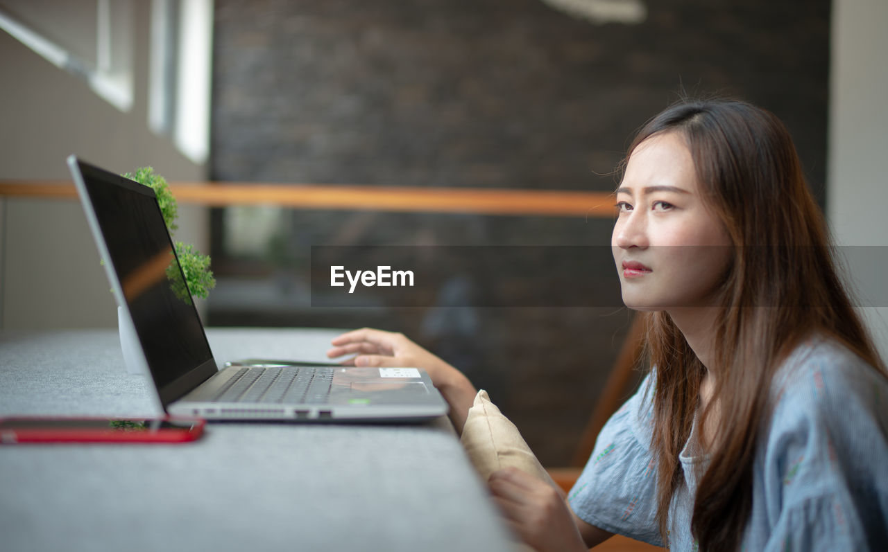 Side view of woman with laptop on sofa looking away at home