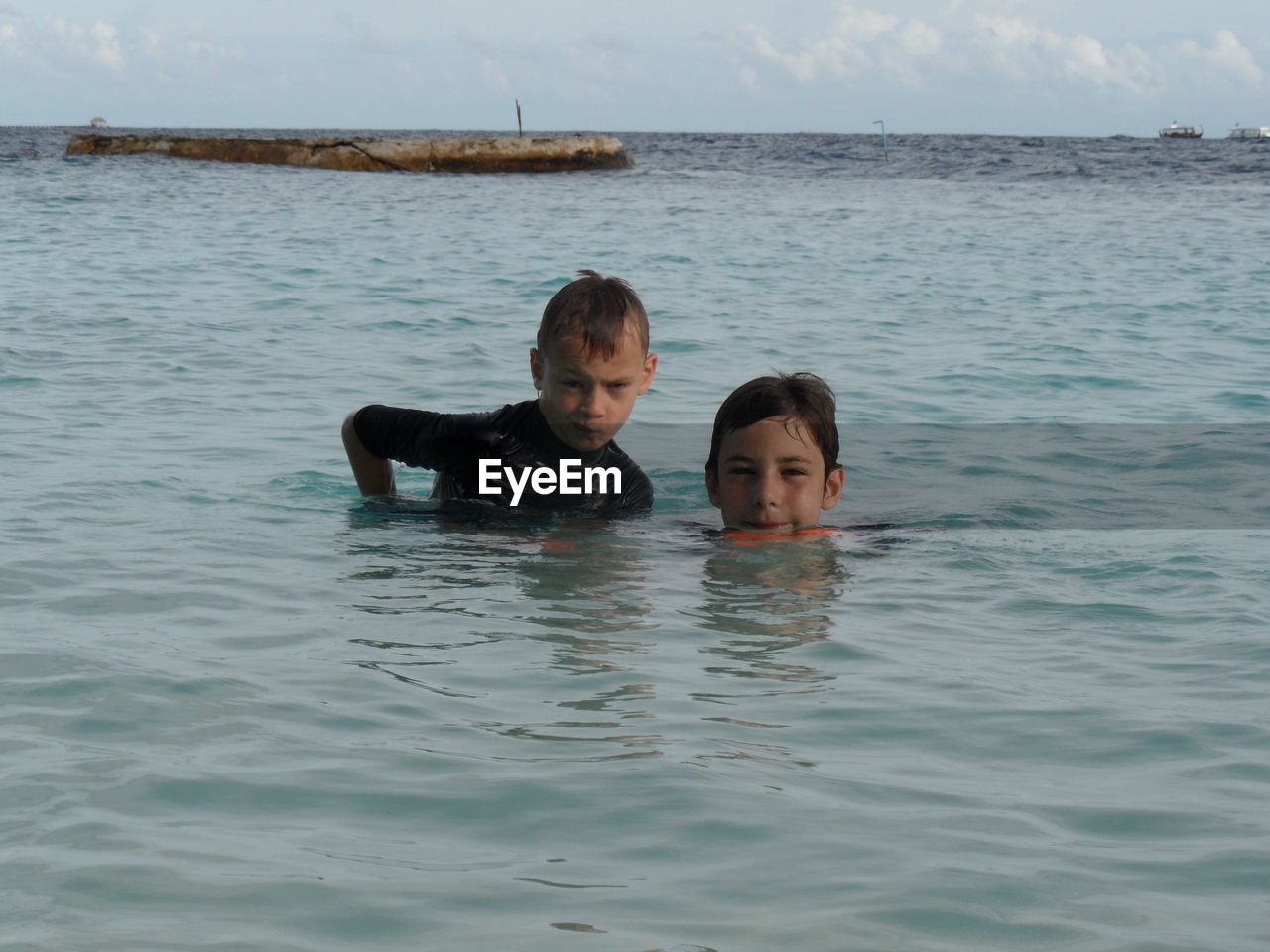 Portrait of brothers swimming in sea against sky