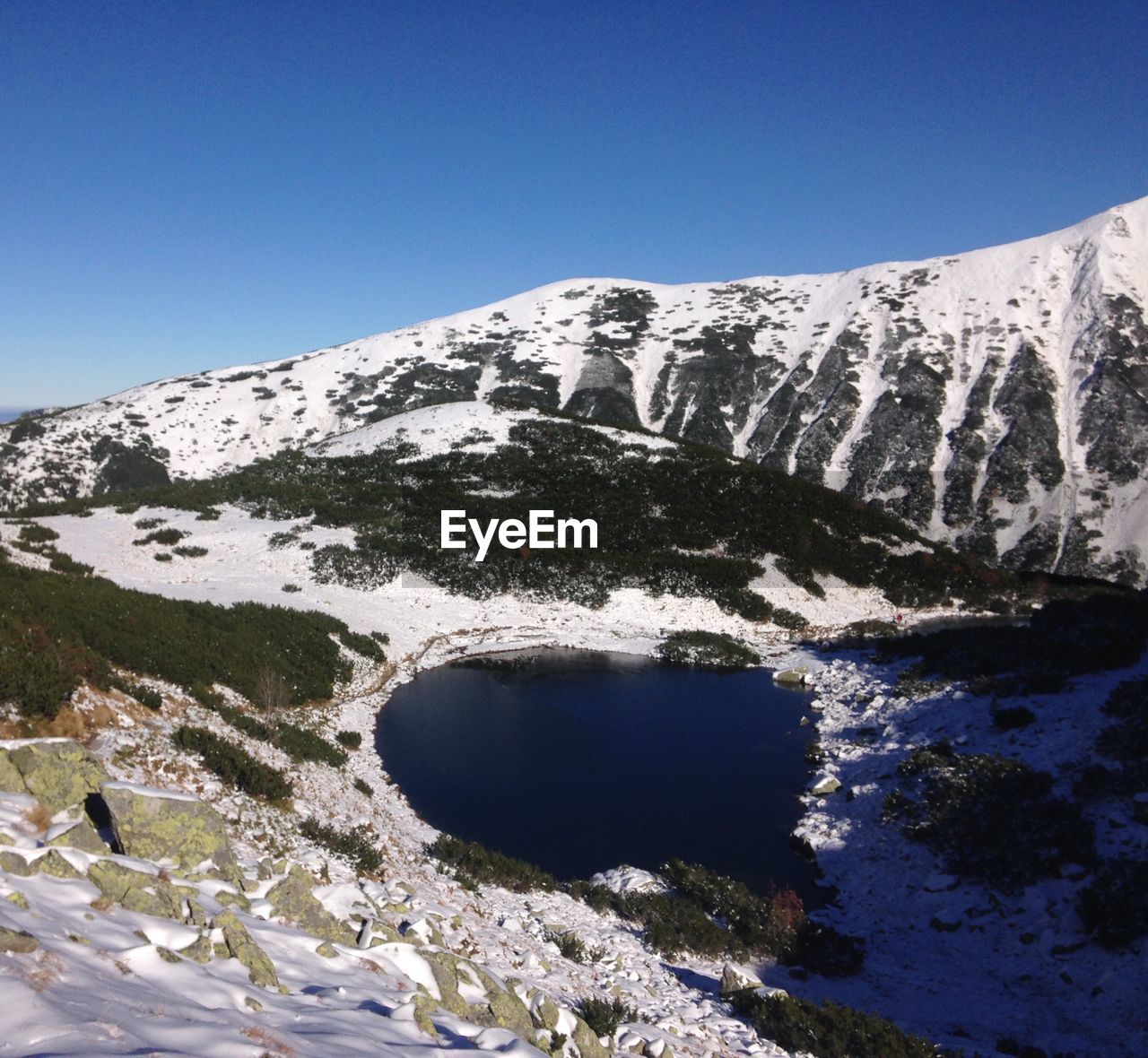High angle view of lake amidst snowcapped mountains against clear blue sky