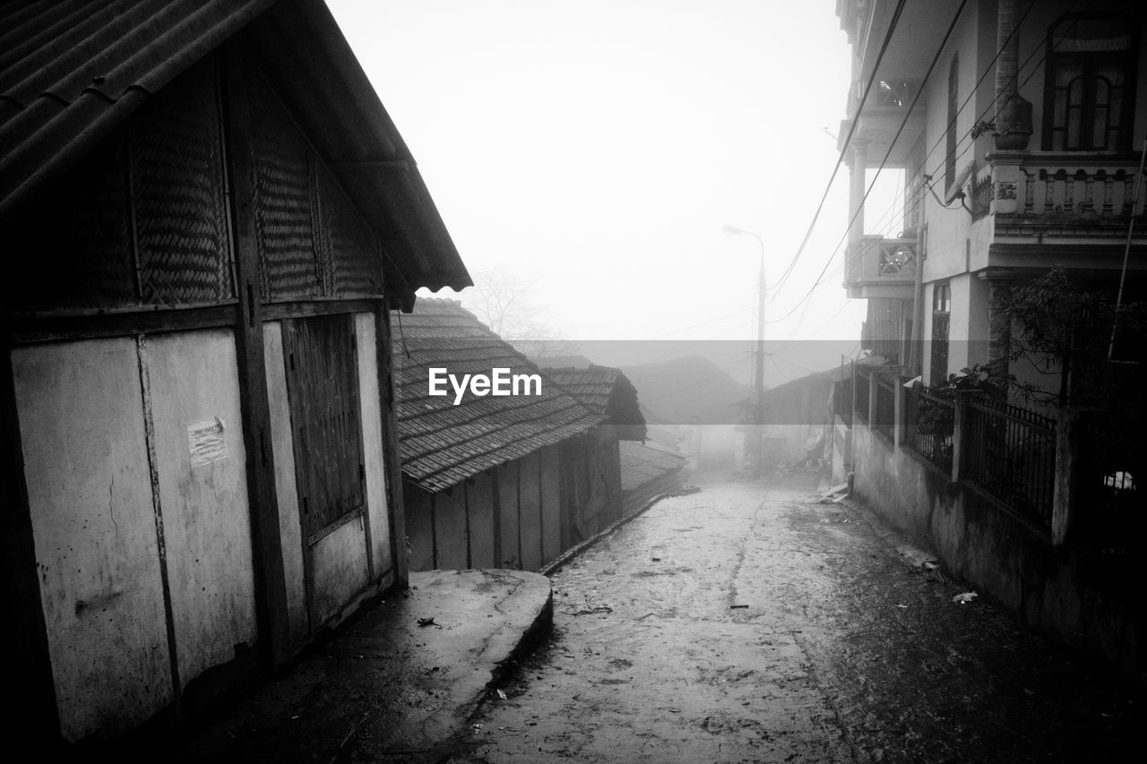 Wet street amidst houses during foggy weather