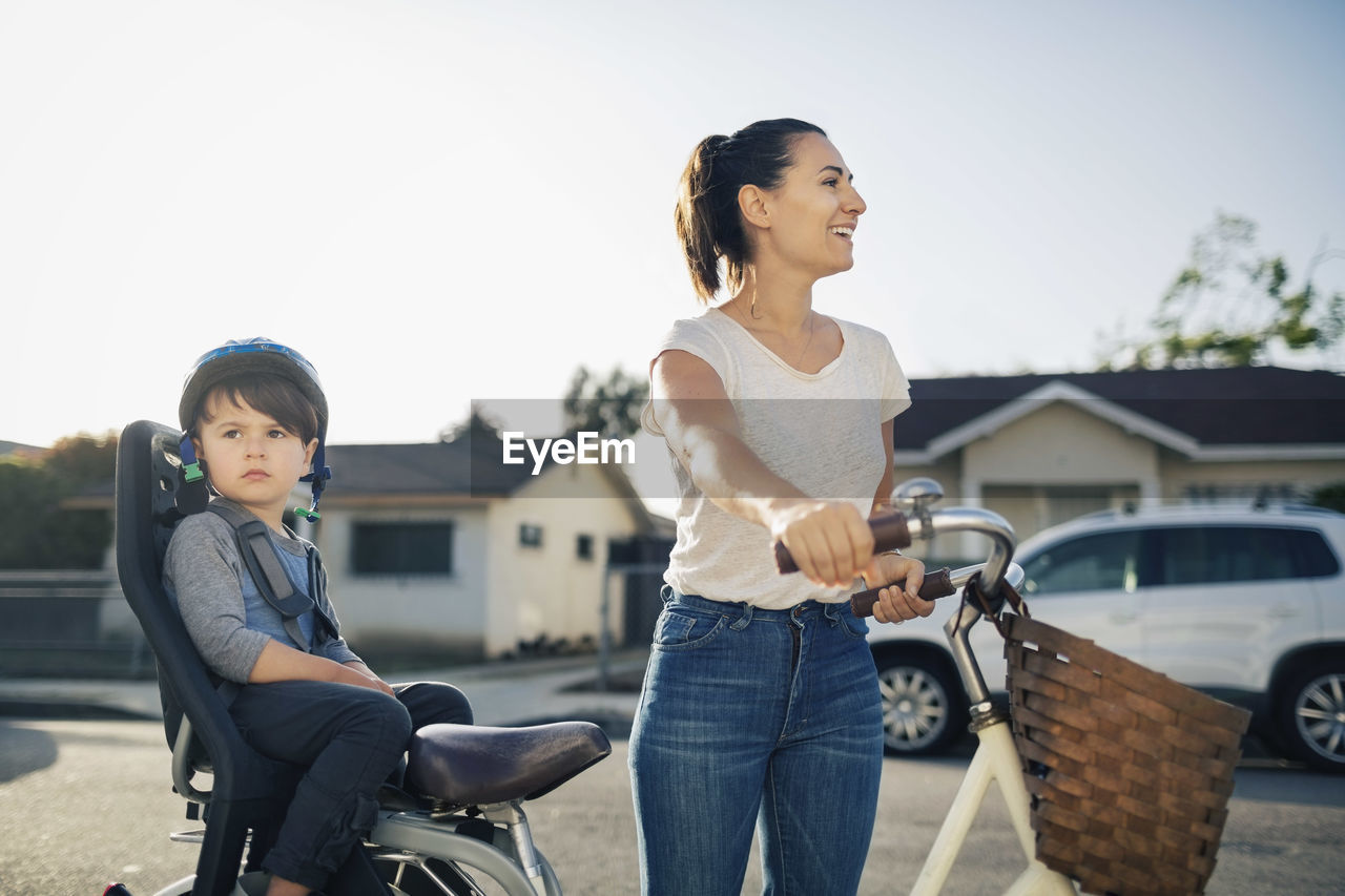 Happy woman looking away while son sitting on bicycle outdoors