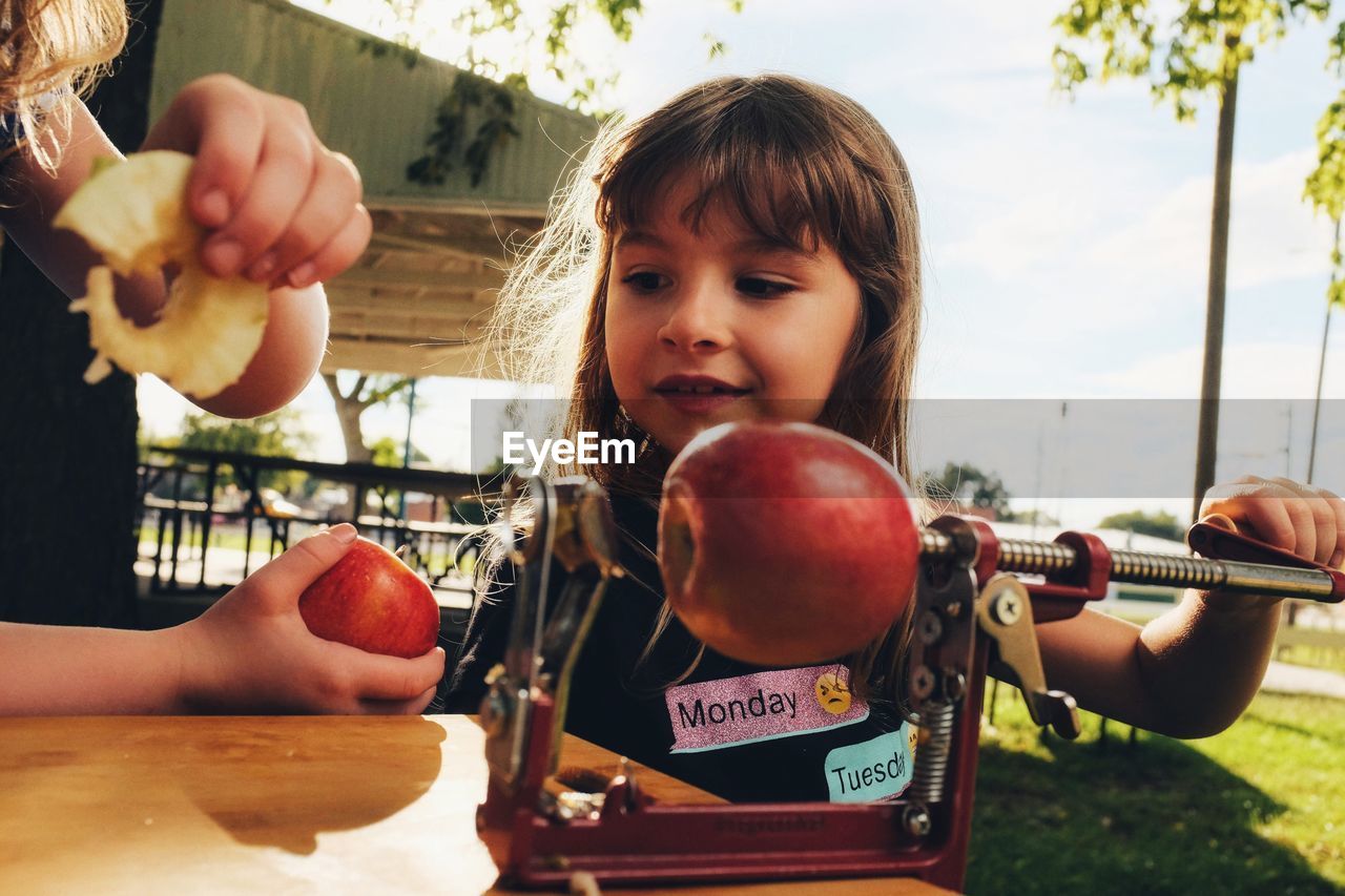 Cute girl holding fruit peeler on table outdoors