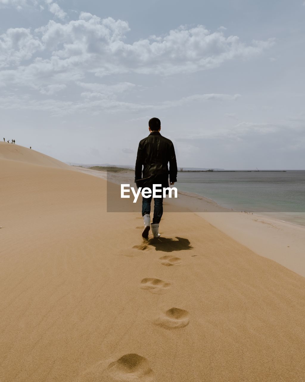 Rear view of man walking on sand dune by beach