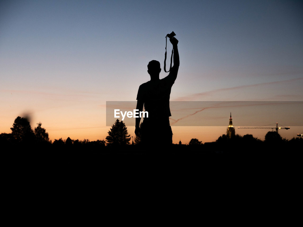 Silhouette man with camera standing against sky during sunset