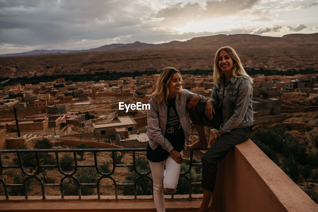 Smiling friends spending leisure time on building terrace against sky