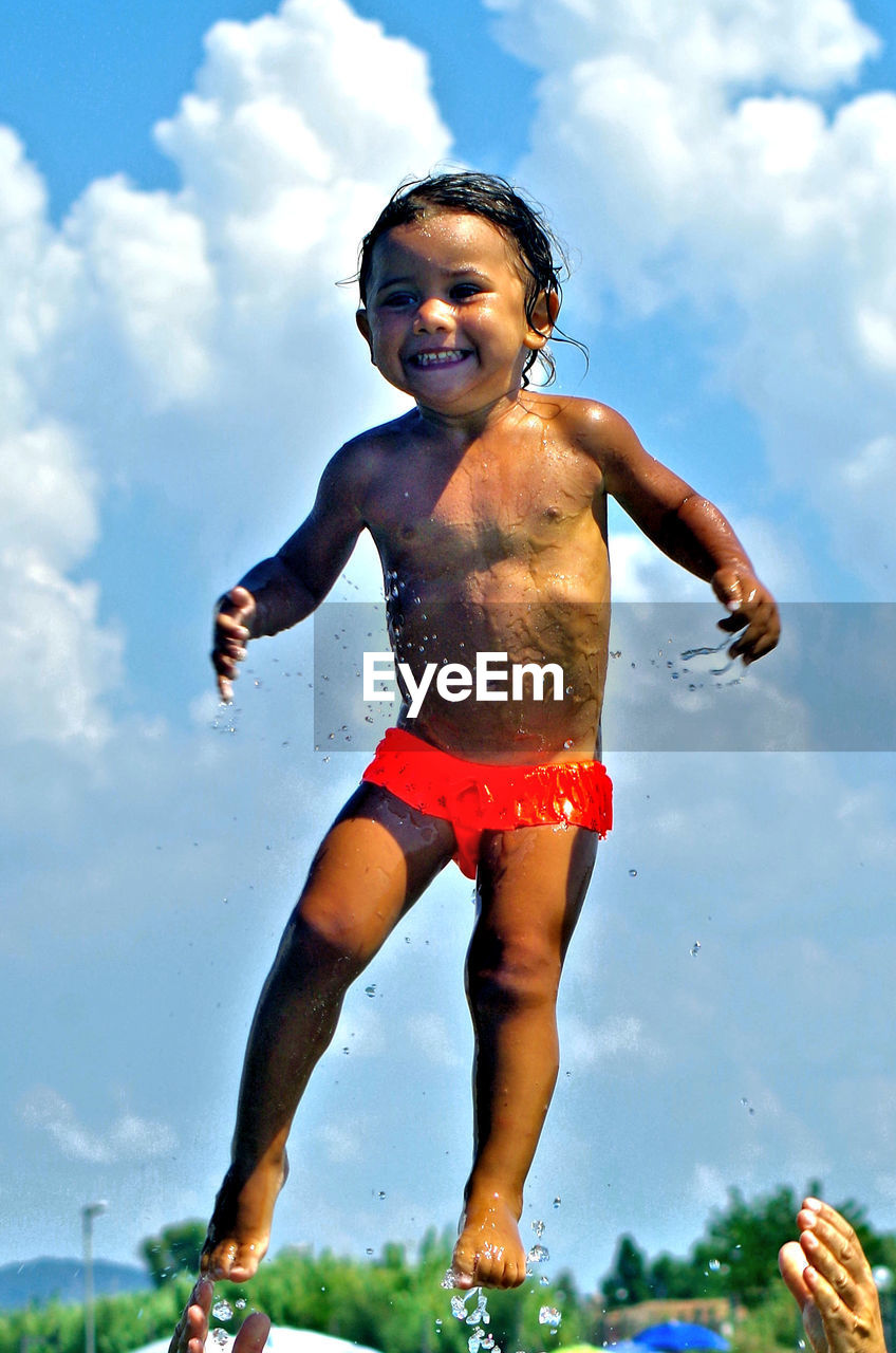 Full length of shirtless boy jumping against sky