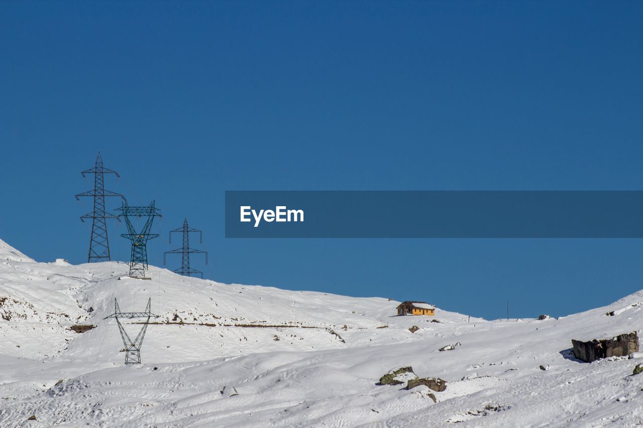 Electricity pylon on snow covered landscape against clear blue sky