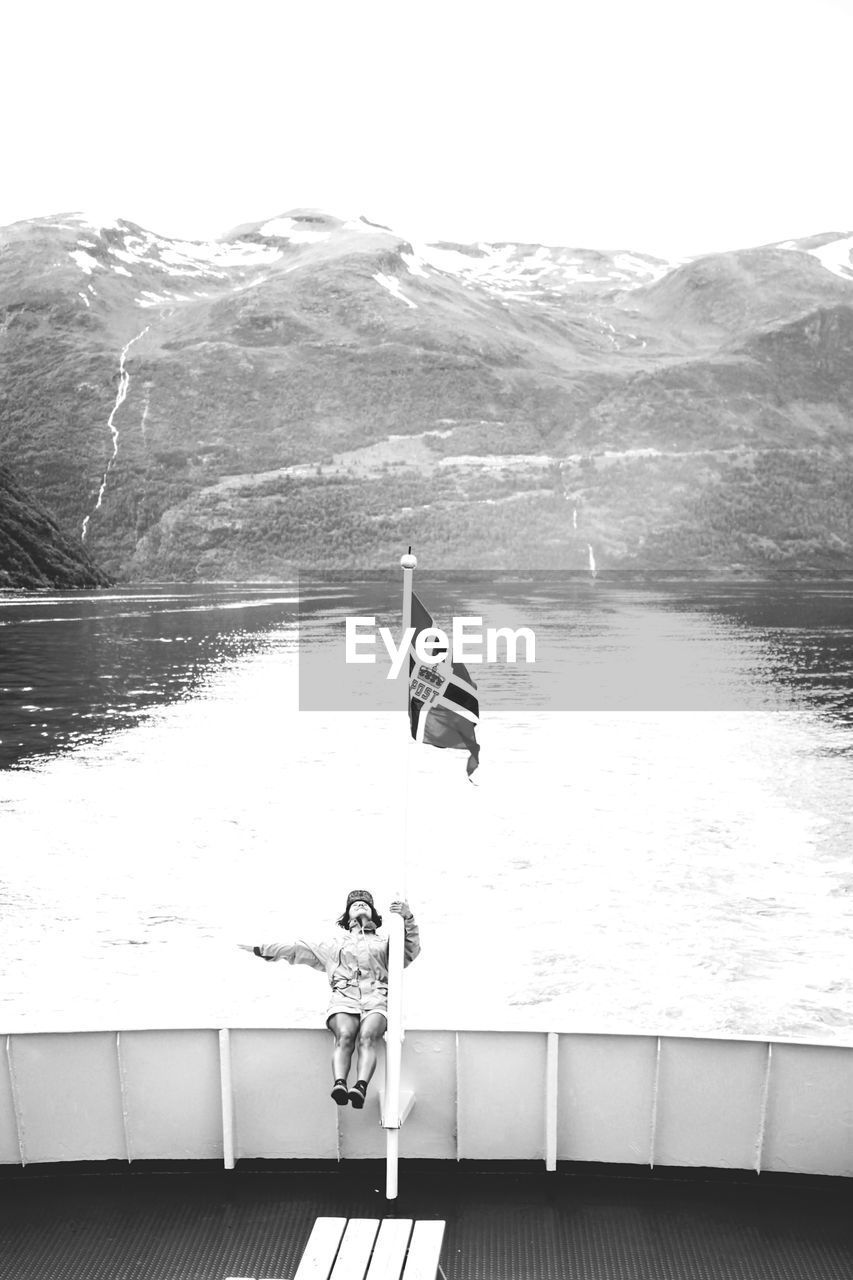 Full length of person by norwegian flag on boat railing at sea
