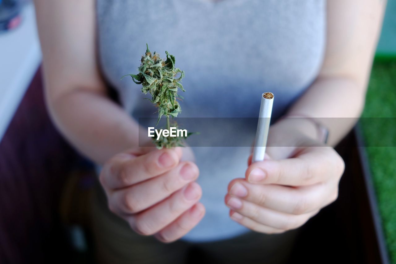Close-up of woman holding cigarette and cannabis plant