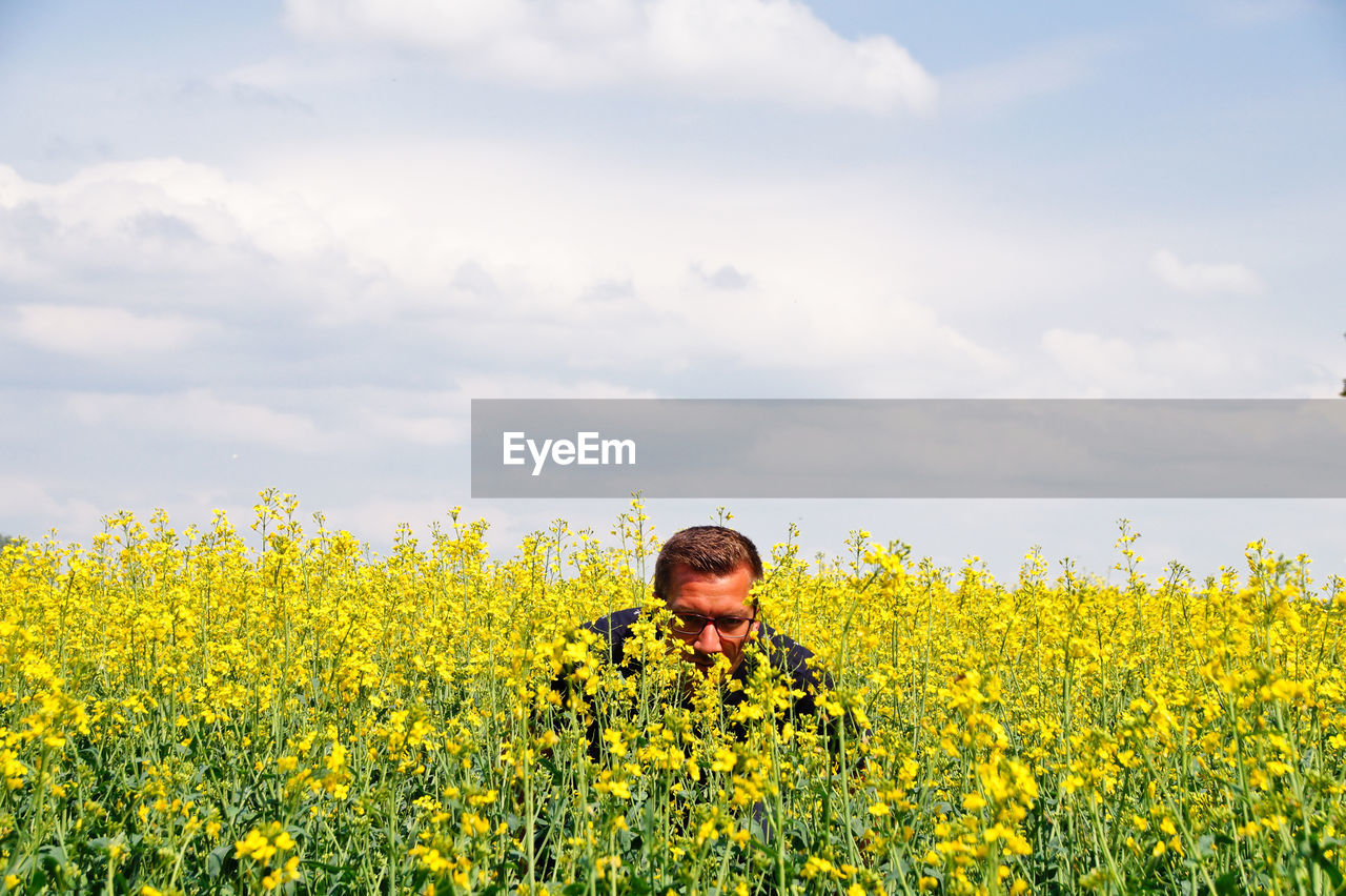 Portrait of mid adult man in oilseed rape field against cloudy sky