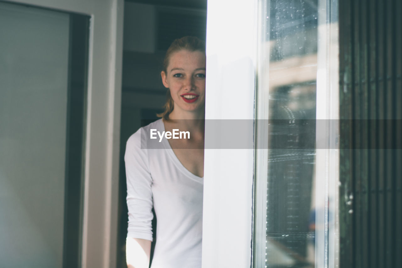 Portrait of happy young woman standing at house entrance