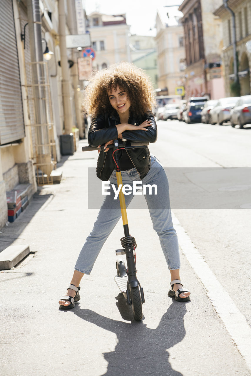 Portrait of smiling teenage girl standing with scooter on pavement