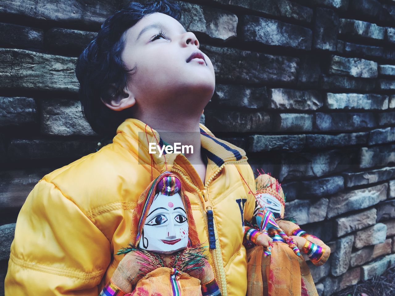 Boy holding puppets and standing against wall